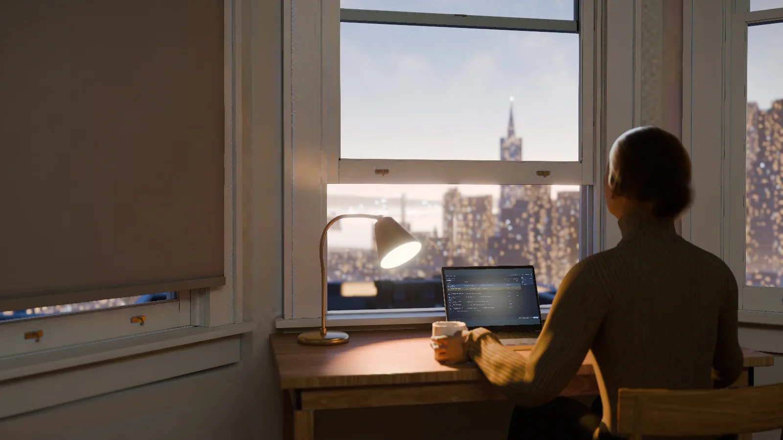 A person seen from behind at a desk by a tall window at dawn, a laptop open in front of her and the lit city outside